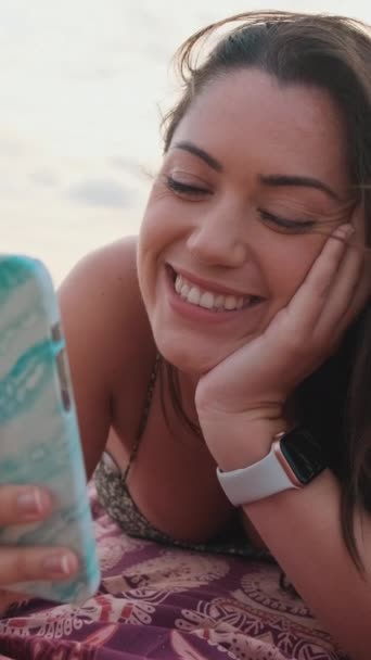关门吧 年轻女人在海滩上放松的时候用的是智能手机 女孩抬起头 微笑着看着摄像机 — 图库视频影像