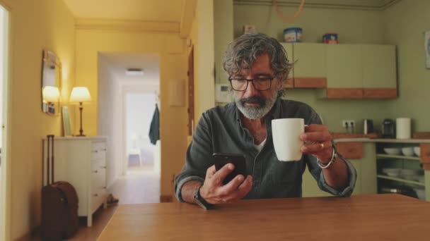 Anciano Bebe Café Taza Utiliza Teléfono Móvil Casa — Vídeos de Stock