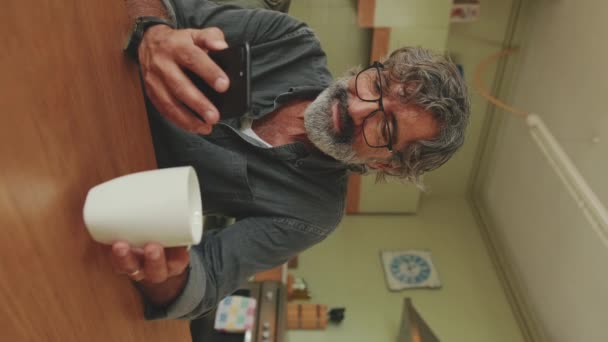 Video Vertical Anciano Complacido Bebe Café Taza Usa Teléfono Móvil — Vídeos de Stock