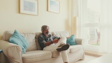 Uzaktan kumandalı yaşlı adam evdeki kanepede oturuyor.