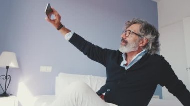 Adam yatakta oturur ve selfie çeker.