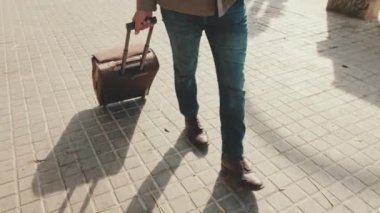 Sokakta bavulla yürüyen orta yaşlı bir adamın bacakları yakın plan.