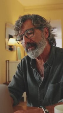 Ev mutfağında oturan ve dizüstü bilgisayarda yazan yaşlı, pozitif bir adam.