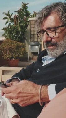 Olgun bir erkek balkonda otururken cep telefonu kullanır.