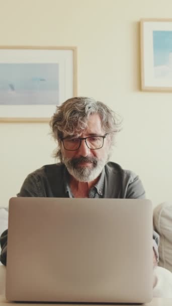真实的视频 年长的 积极的男人坐在客厅沙发上的笔记本电脑上打字 — 图库视频影像