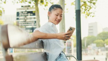 Genç kadın bankta oturuyor ve cep telefonu kullanıyor.