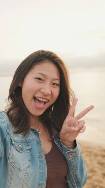 Genç ve güzel bir kadın deniz manzarasında dururken selfie çekiyor.