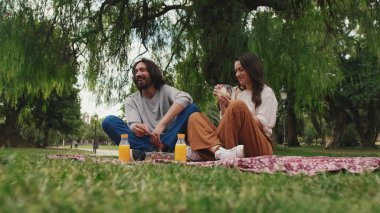 Gülen çift parkta pikniğin tadını çıkarıyor.