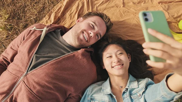 快乐的夫妇在公园里躺在毛毯上自拍 顶部视图 — 图库照片