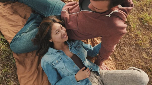 Dışarıda, parkta battaniyeye uzanmış genç bir çiftin yakın çekimi. Üst görünüm