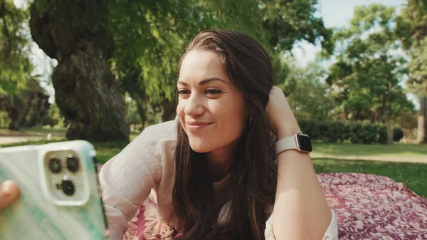 公園でリラックスして携帯電話からビデオ通話をする若い女性 — ストック写真