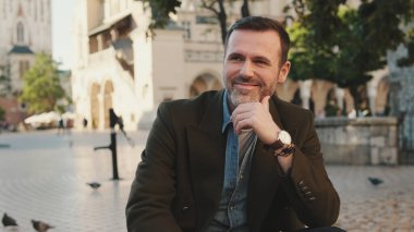 Kameraya bakıp gülümseyen bir adam.