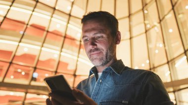 Yakın plan, orta yaşlı adam akşamları iş merkezinin yanında cep telefonu kullanıyor.