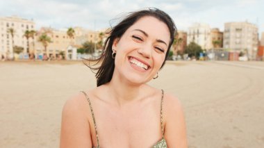 Genç kadın sahilde duruyor ve uzaklara bakıyor. Kız başını çevirir, kameraya bakar ve gülümser.