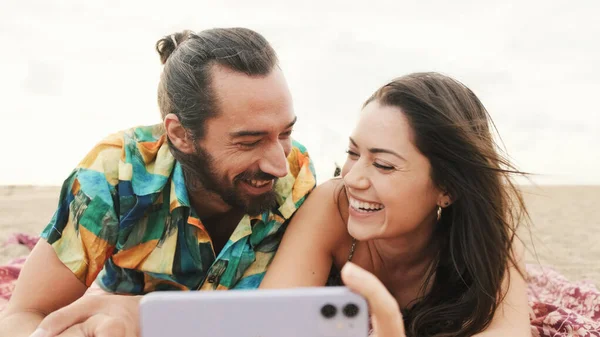 情侣们在沙滩上放松 在手机上看视频和照片 — 图库照片