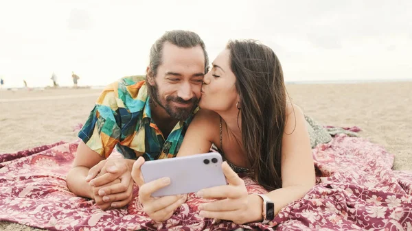 恋爱中的夫妻躺在沙滩上亲吻 在手机上自拍 — 图库照片