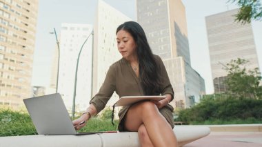 Genç kız dizüstü bilgisayar kullanıyor. Dışarıdan modern binalar hakkında notlar alıyor.