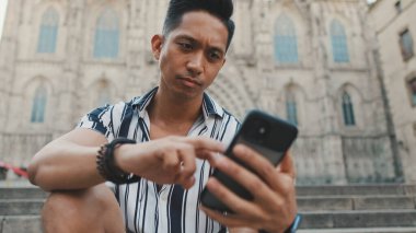 Basamaklardaki genç turist, arka planda otururken cep telefonu kullanıyor