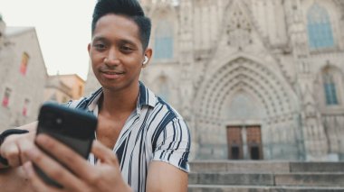 Basamaklardaki genç turist, arka planda otururken cep telefonu kullanıyor