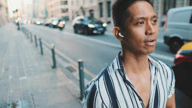 Genç adam yolun kenarında yürüyor ve kulaklıkla müzik dinliyor.