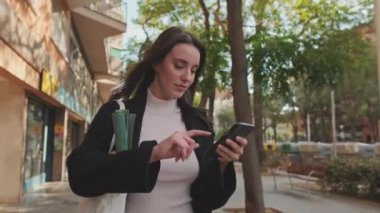 Güzel genç bir kadın markette poşetle sokakta yürüyor ve cep telefonu kullanıyor.
