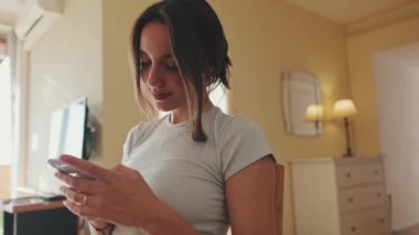 Mutfakta otururken cep telefonuyla fotoğraf çeken gülümseyen genç bir kadının yakın çekimi.