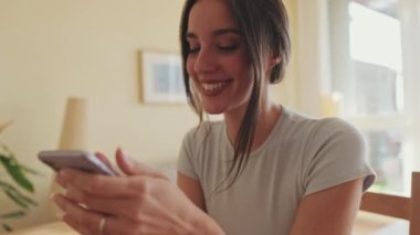 Mutfakta otururken cep telefonuyla fotoğraf çeken gülümseyen genç bir kadının yakın çekimi.