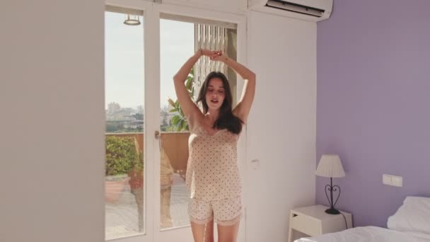 穿着睡衣的年轻女人站在卧室的窗边时伸懒腰 — 图库视频影像