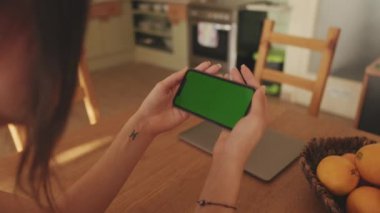 Evde cep telefonu yeşil ekran krom anahtarı kullanan genç bir kadının ellerini yakın plan çek.