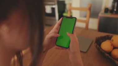 Evde cep telefonu yeşil ekran krom anahtarı kullanan genç bir kadının ellerini yakın plan çek.