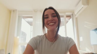 Evde otururken bilgisayarla konuşan genç bir kadın.