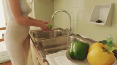 Ön plandaki kasede taze sebzeler, arka plandaki kız sebzeleri yıkar.