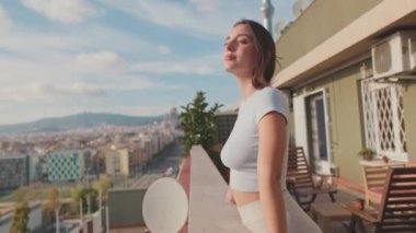 Genç bir kadın balkonda dikilirken güzel manzaranın tadını çıkarıyor.