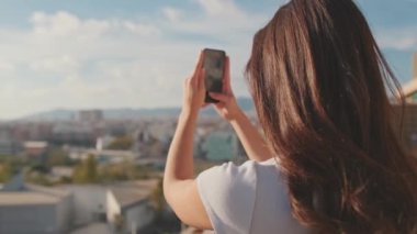 Kapatın, genç bayan cep telefonuyla fotoğraf çekiyor evdeki balkonda dikilirken. Arka plan