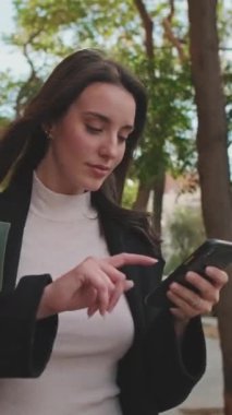 VERTICAL VIDEO, güzel genç bir kadın markette poşetle sokakta yürüyor ve cep telefonu kullanıyor.