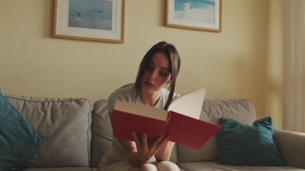 Mujer Joven Leyendo Libro Sentado Sofá Casa — Vídeo de stock