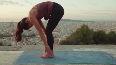 Genç bir kadın gün doğumunda izleme platformunda yoga yapıyor.