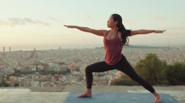 Genç bir kadın gün doğumunda izleme platformunda yoga yapıyor.