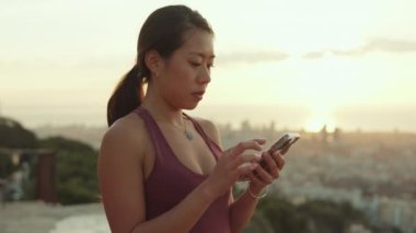 Young athletic woman using mobile phone while standing at lookout point at dawn