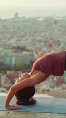 VERTICAL VIDEO: Young woman practicing yoga, lifting pelvis while lying on mat on viewing platform