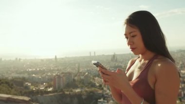 Kapalı, mutlu atletik kadın gözetleme noktasında dururken cep telefonu kullanıyor.