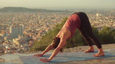 Genç bir kadın gün doğumunda izleme platformunda yoga yapıyor. Amanho mukha svanasana pozu