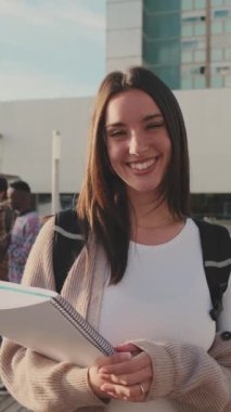 Student with notebooks in her hands looks at the camera and smiles