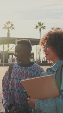 Cheerful students are talking and laughing standing outside with books