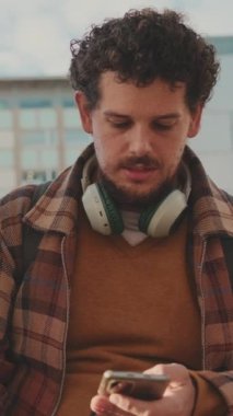 Guy student sits next to the building of the university, uses a mobile phone