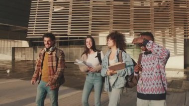 Happy diverse students chatting and laughing walk together down the street to the university