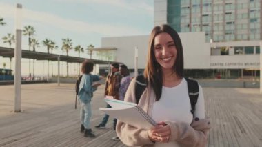 Student with notebooks in her hands looks at the camera and smiles