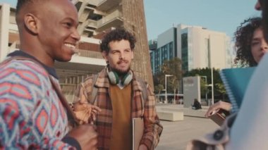 Four young students stand on sunny street communicating sharing stories laughing enjoying funny company