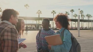 Cheerful students are talking and laughing standing outside with books