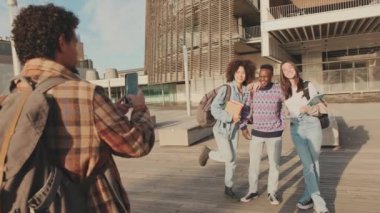 Group of students smiling while looking at mobile phone camera while standing outside
